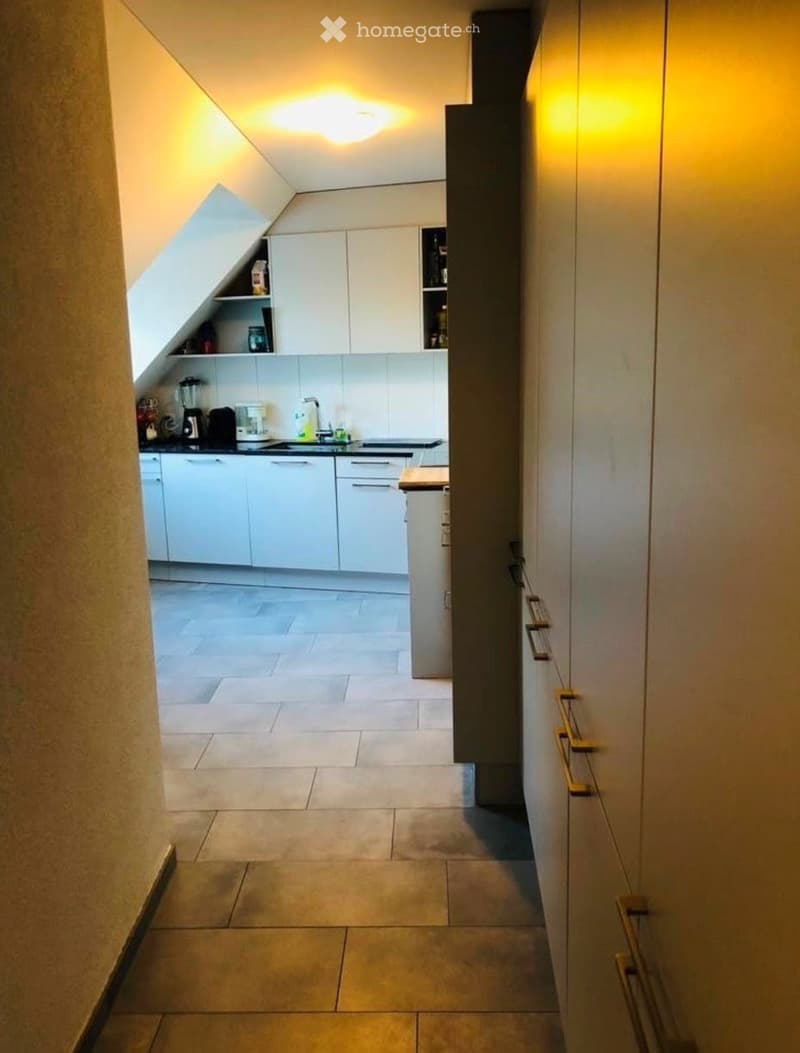 Modern kitchen with white cabinets, a blender, coffee maker, and a sink, featuring a tiled floor and warm lighting.