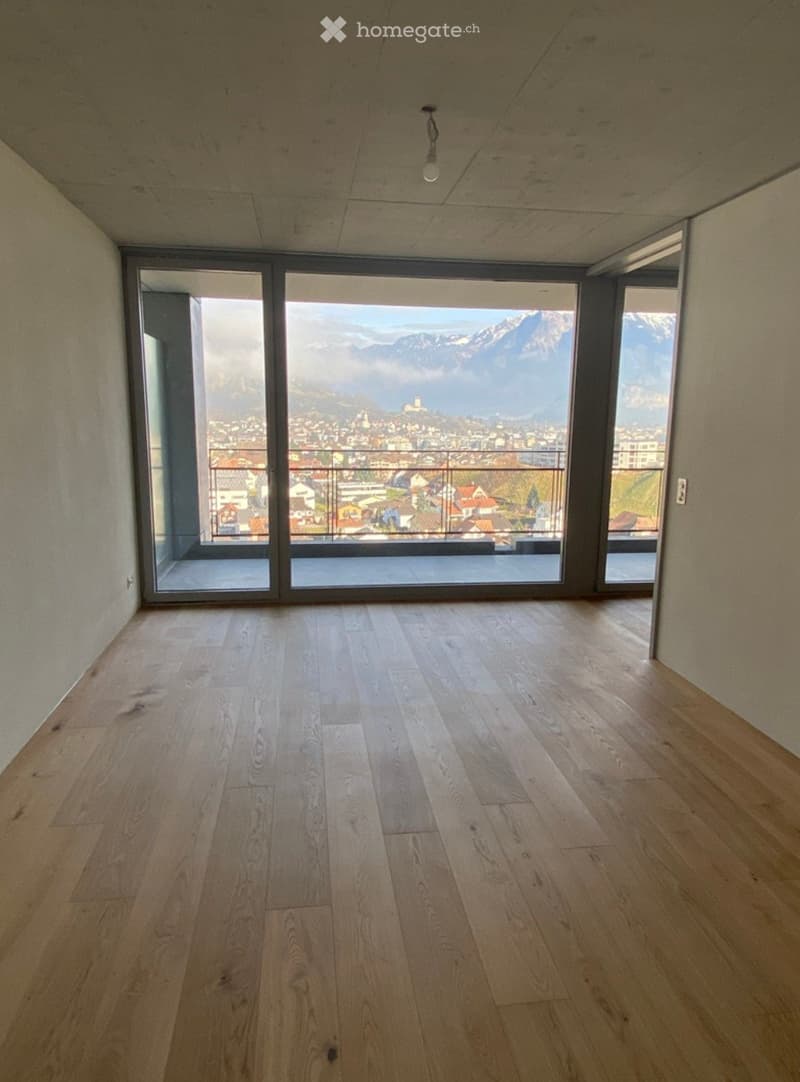 Empty room with light wooden flooring and large windows offering a scenic mountain view.
