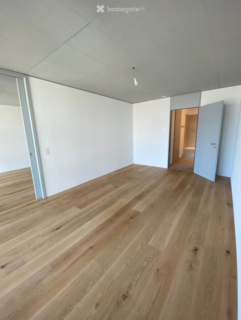 Empty room with light wooden flooring, white walls, and a visible doorway leading to another space.