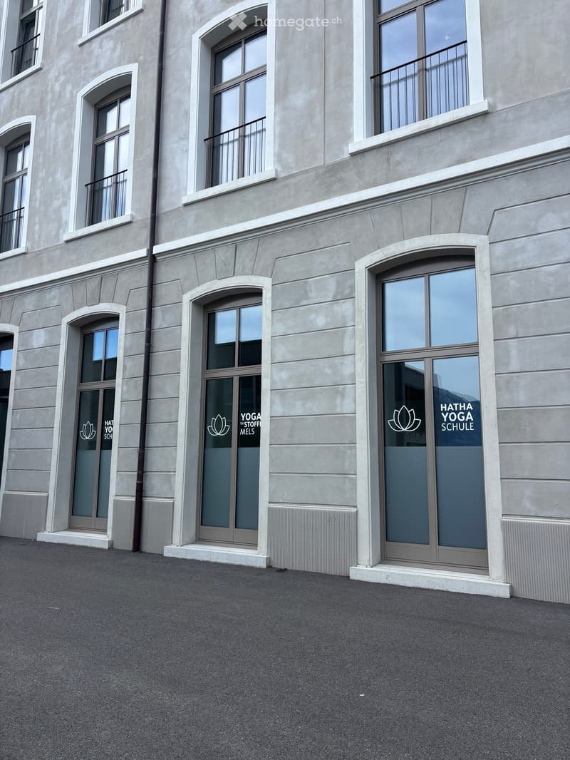 Modern building facade with large windows and arched doorways, featuring yoga school signage.