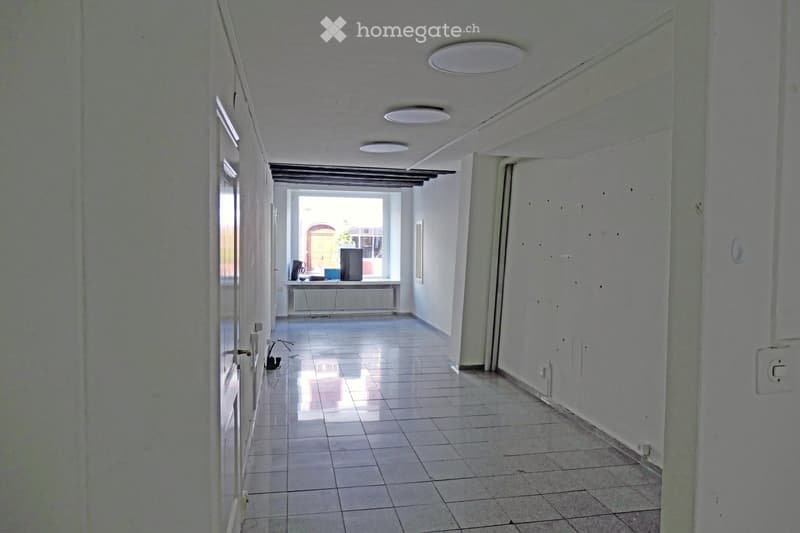 Empty hallway with tiled floor, white walls, and several ceiling lights. Doors on both sides lead to other rooms.