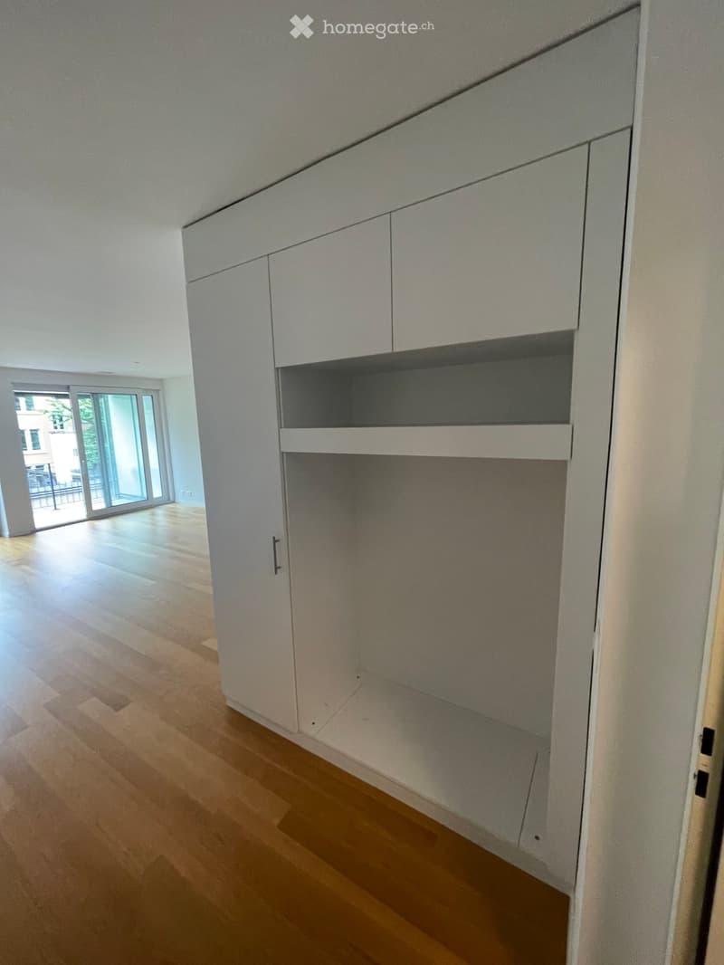 Empty room with light wooden flooring, white walls, and built-in white cabinets with open shelving.