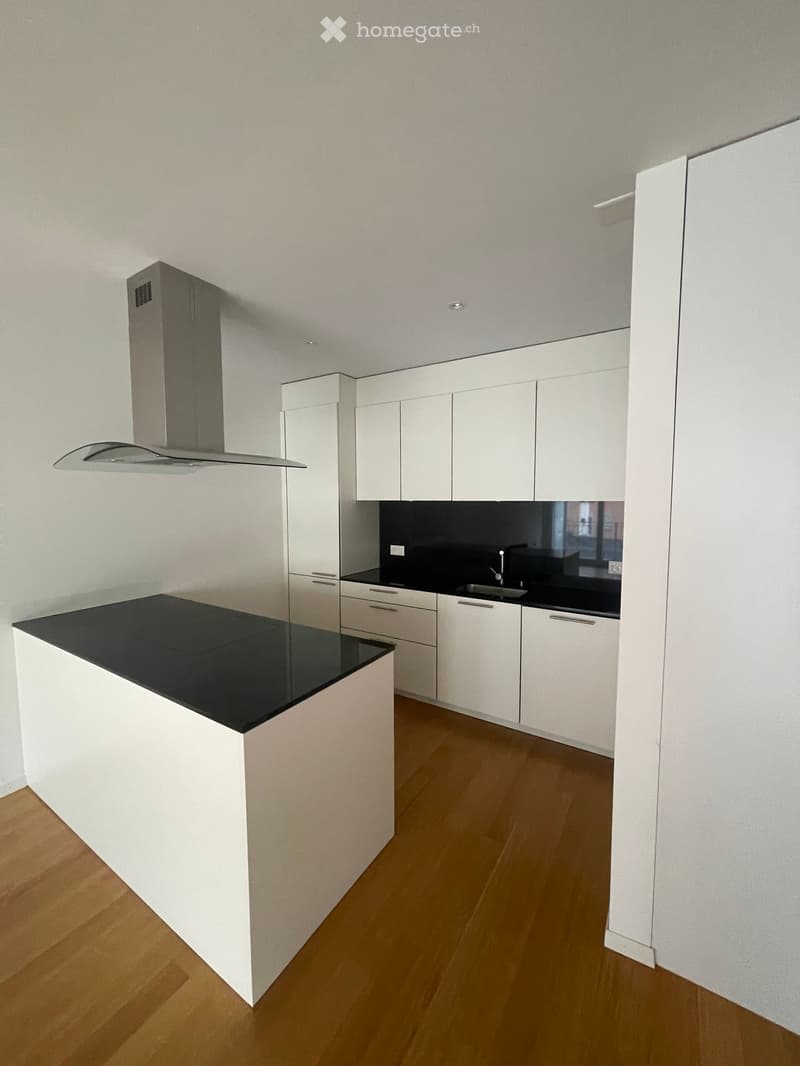 Modern kitchen with white cabinets, black countertops, a central island, and a range hood.