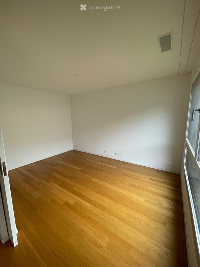 Empty room with light-colored walls and wooden flooring, featuring a window with a white frame and a door with a silver handle.