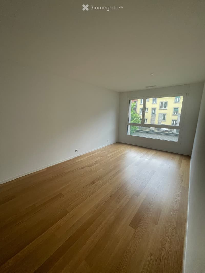 Empty room with wooden flooring and large window showing a cityscape view.