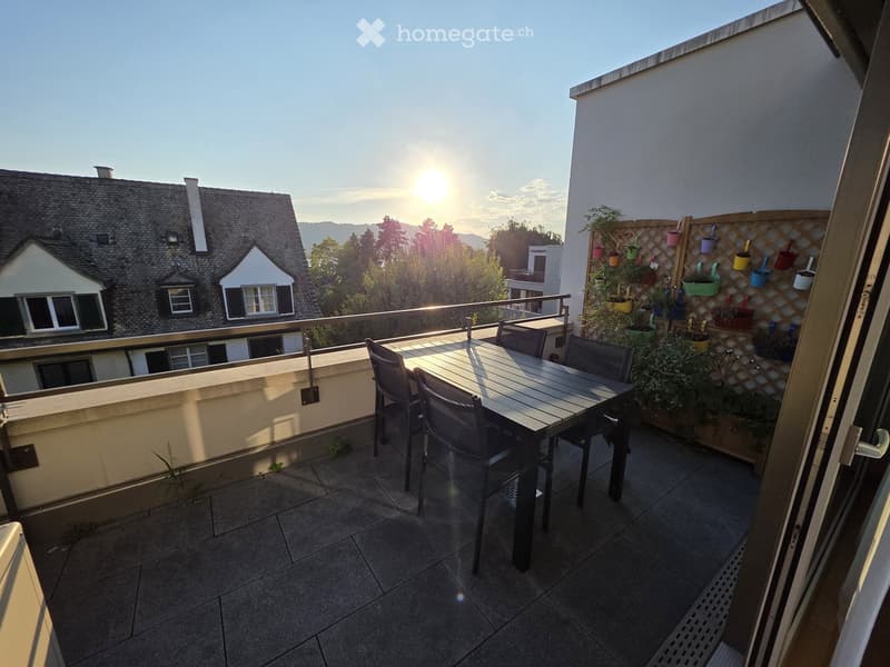 Balcony with a table and chairs, overlooking a residential area with houses and trees.