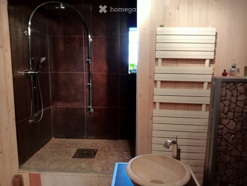 Modern bathroom with a glass-enclosed shower, a stone sink, a radiator, and a small window letting in natural light.