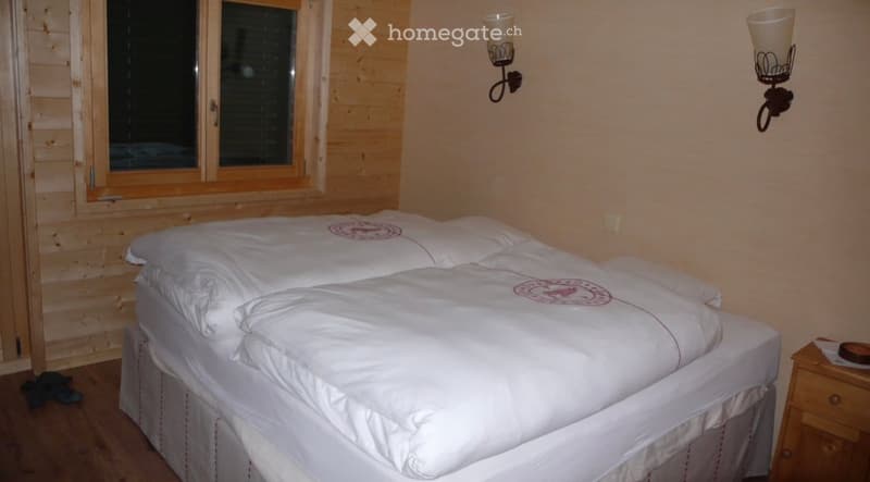Cozy bedroom with wooden walls, a large bed with white bedding, and a nightstand with a lamp.
