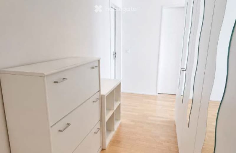 A modern, minimalist bedroom with a white wardrobe, a large mirror, and light wooden flooring.