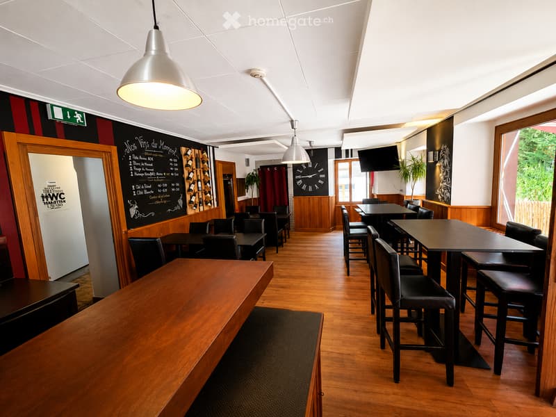 Restaurant interior with wooden floors, black tables, chairs, wine rack, and pendant lights.