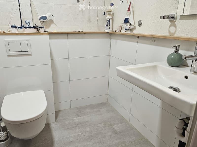 Modern bathroom with white tiles, a toilet, a sink with a chrome faucet, and decorative items on the countertop.