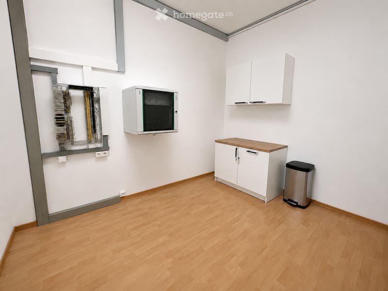 Empty room with light wooden flooring, white walls, and basic built-in cabinets and a small table.