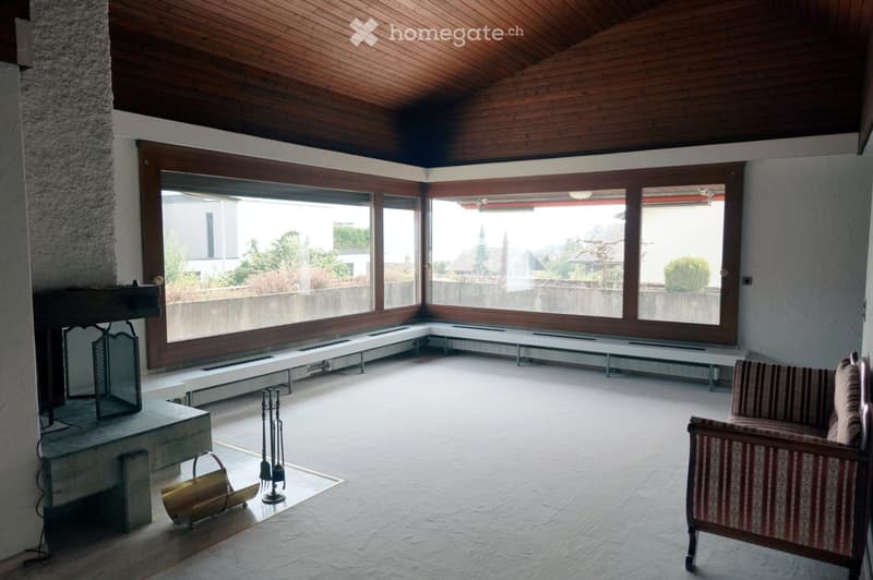 Bright living room with large windows, wooden ceiling, fireplace, and a single sofa.