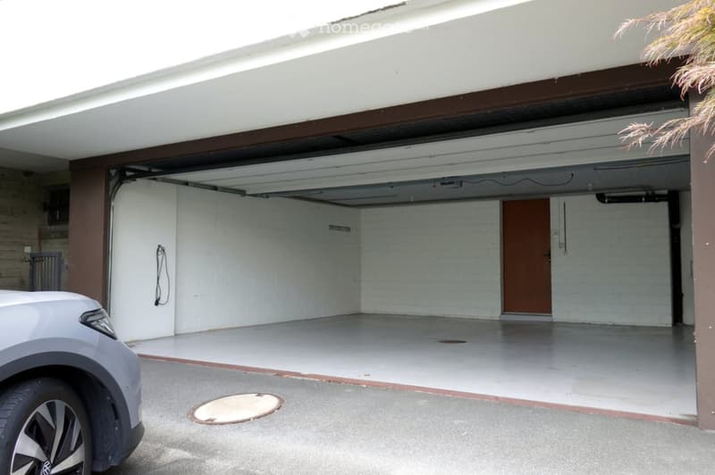 Garage with white brick walls, concrete floor, and a partially open garage door. A car is partially visible in the foreground.