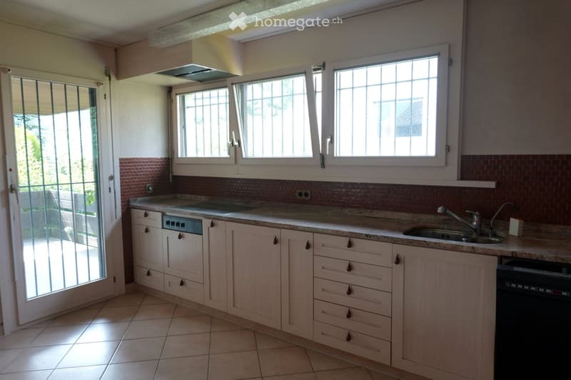 Bright kitchen with light wooden cabinets, granite countertop, sink, and dishwasher. Large windows with blinds provide natural light.