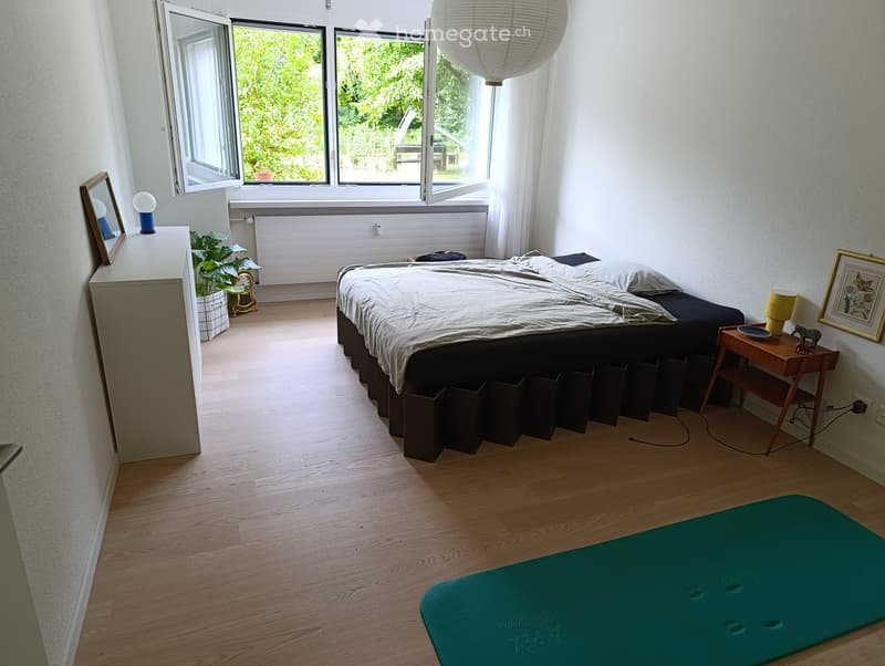 Modern bedroom with a large bed, nightstands, lamps, a potted plant, and a yoga mat on the floor.