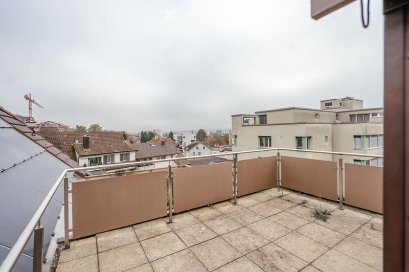 Balcony with tiled floor, metal railing, and brown privacy screens, overlooking a cityscape with buildings and a construction crane.