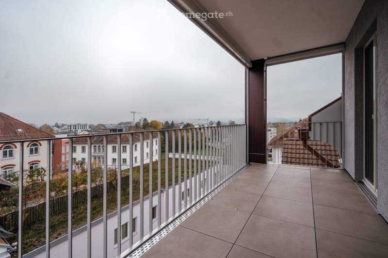 Balcony with modern white metal railing, tiled floor, overlooking a cityscape with residential buildings and autumn foliage.
