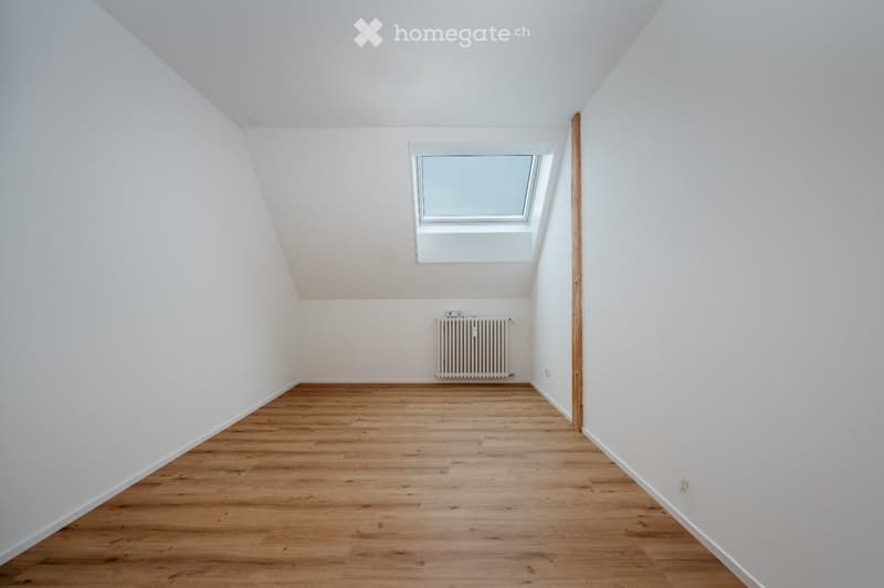 Empty room with wooden flooring, white walls, and a skylight window. A radiator is mounted on the wall.