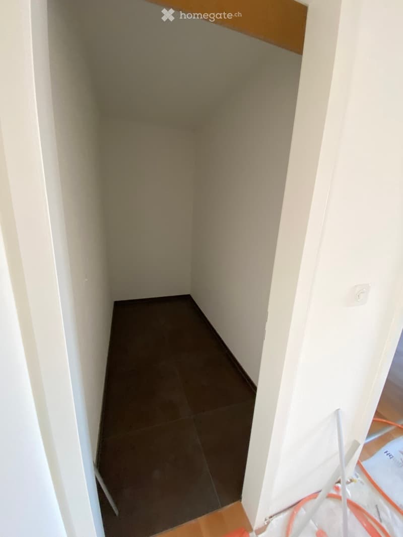 Empty room with beige walls and dark tiled floor, showing a corner view with no furniture or equipment.