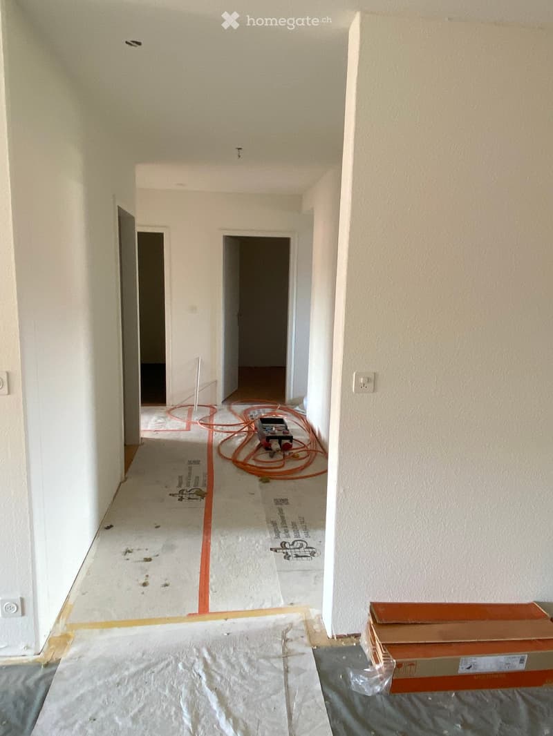 Empty hallway with white walls, exposed wiring, and construction materials on the floor.