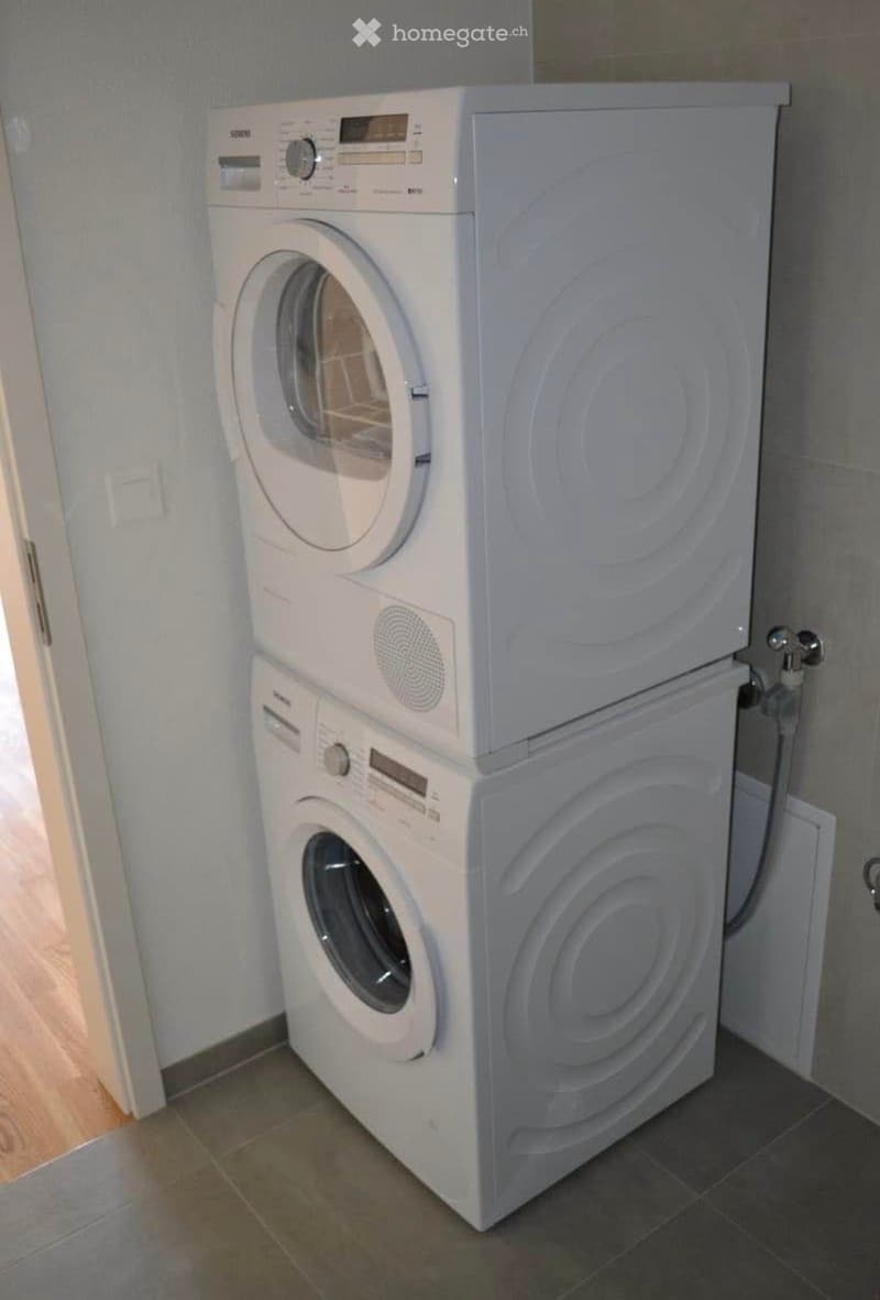 A compact bathroom with a stacked washing machine and dryer unit, featuring a tiled floor and light-colored walls.