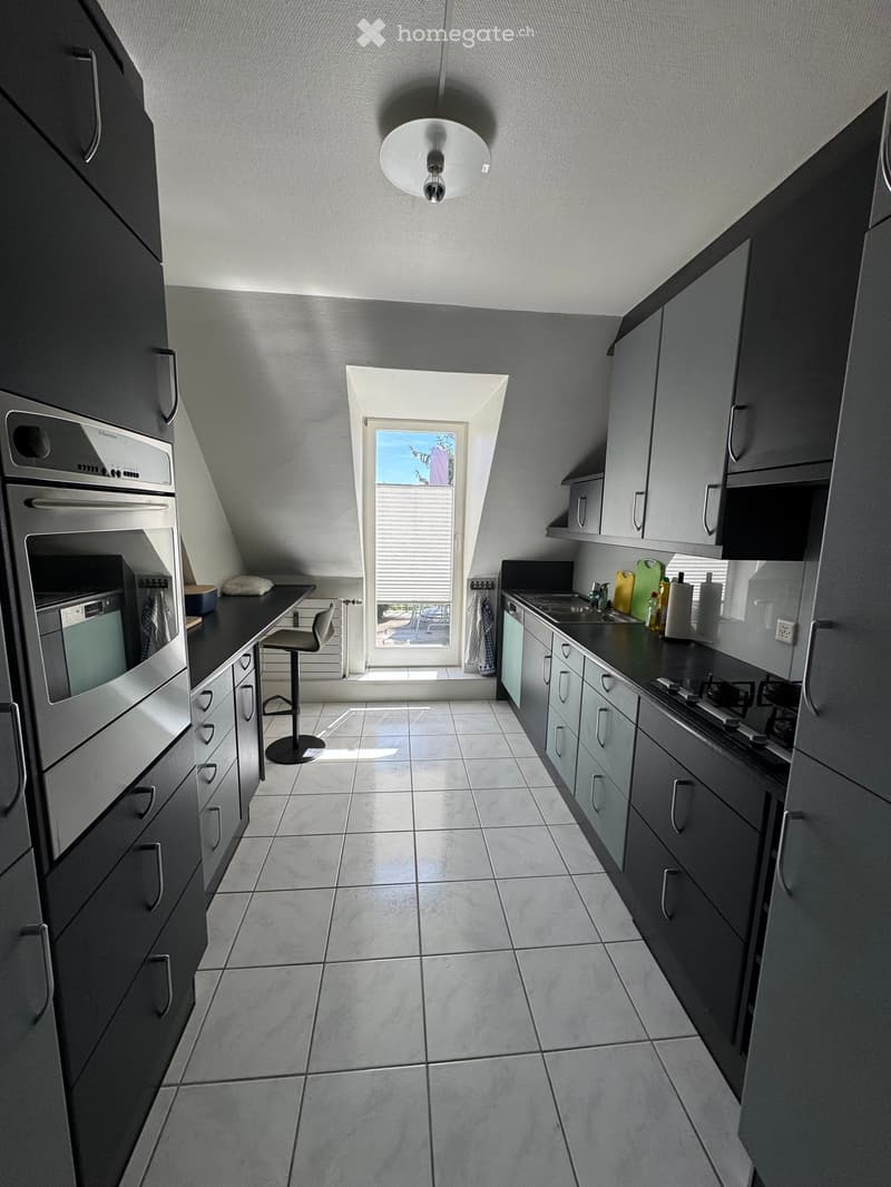 Modern kitchen with grey cabinets, stainless steel appliances, tiled floor, and a skylight window providing natural light.