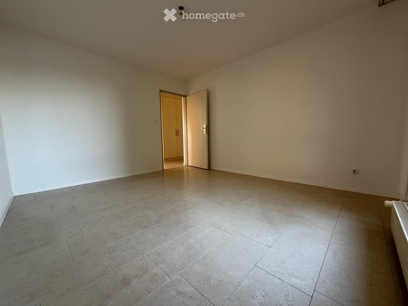 Empty room with light-colored tiled floor and white walls, featuring an open doorway leading to another room.