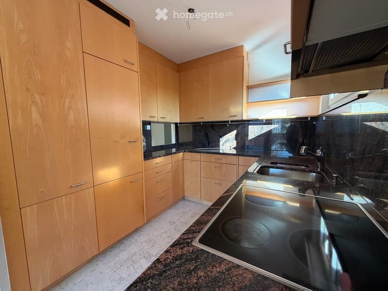 Modern kitchen with light wooden cabinets, granite countertops, stainless steel sink, and electric stove.