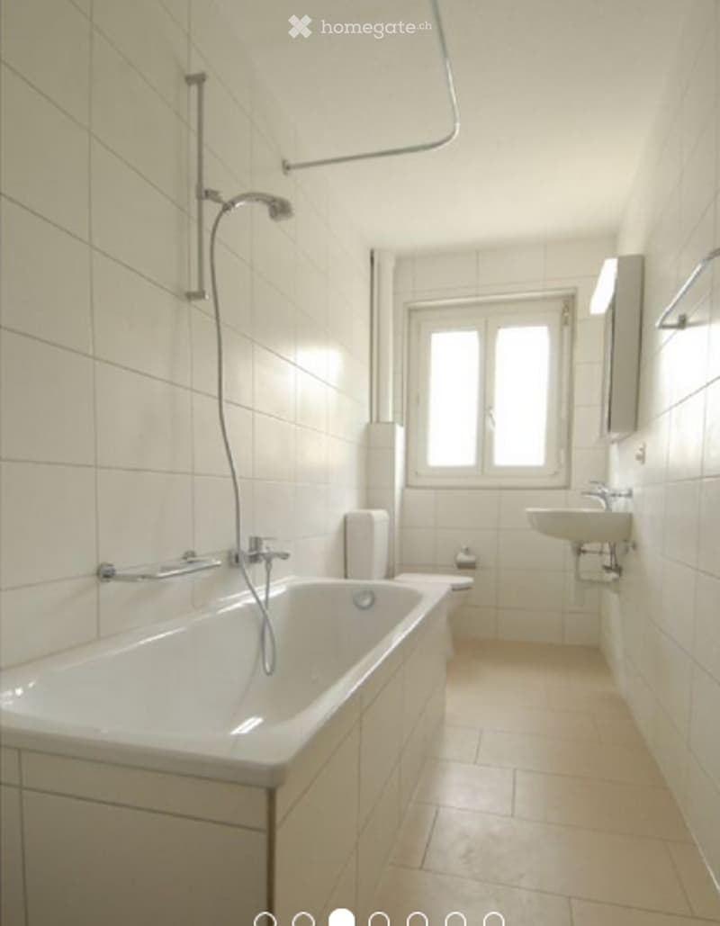 Modern bathroom with white tiled walls and floor, featuring a bathtub, toilet, sink, and mirror.