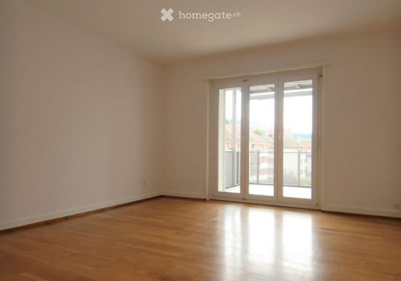 Completely empty room with wooden flooring and large sliding glass doors leading to a balcony.