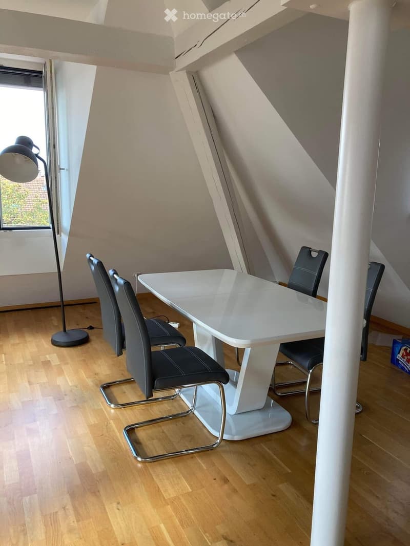 Bright room with wooden flooring, white table, four black chairs, and a floor lamp near a window.