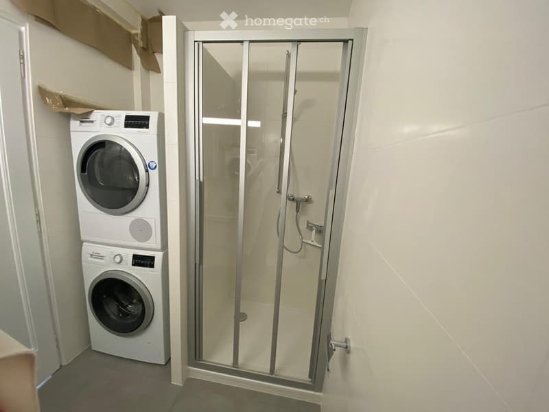 Bathroom with a glass-enclosed shower and a stacked washing machine and dryer unit.