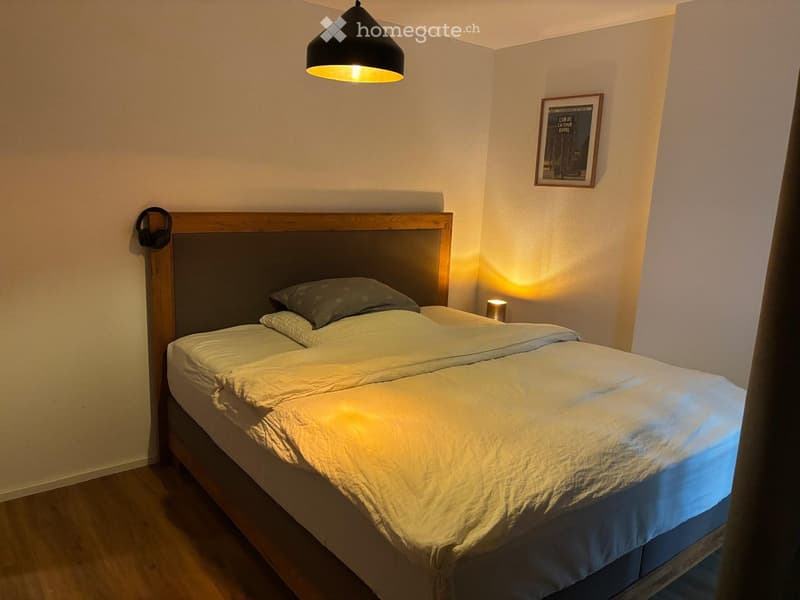 Cozy bedroom with a neatly made double bed, wooden headboard, bedside lamp, and a framed picture on the wall.
