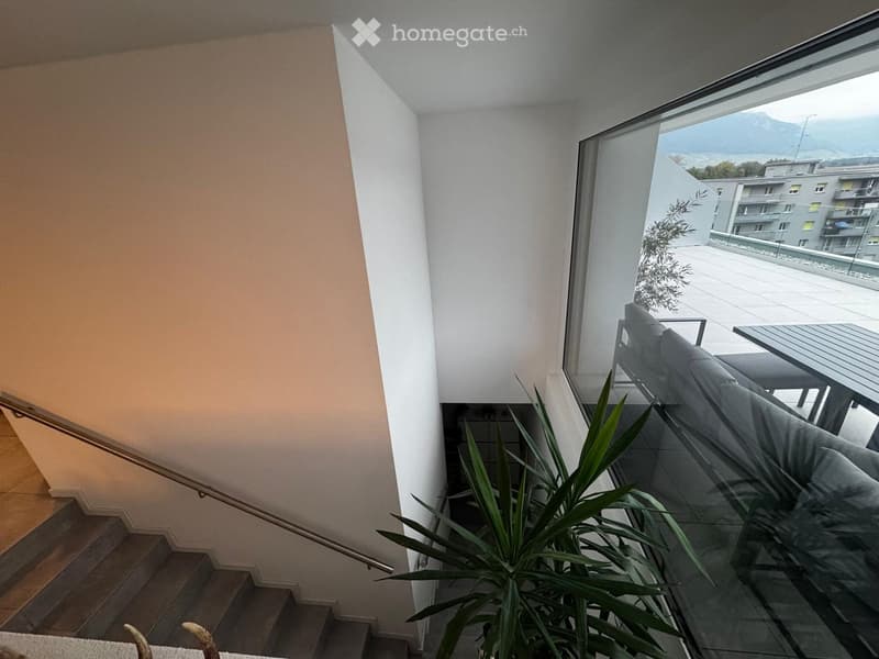 Modern hallway with a staircase leading upwards, large window offering a scenic mountain view, and a potted plant near the window.