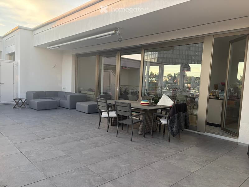 Balcony with tiled floor, grey sofa, ottoman, dining table, and chairs.