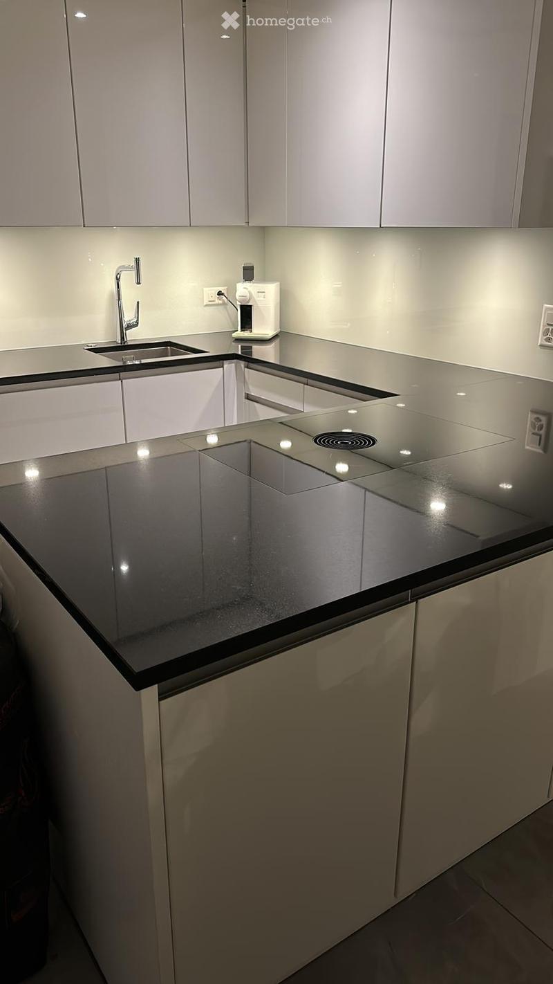 Modern kitchen with sleek white cabinets, a black countertop, and an induction cooktop. Features a stainless steel faucet and a coffee maker on the counter.