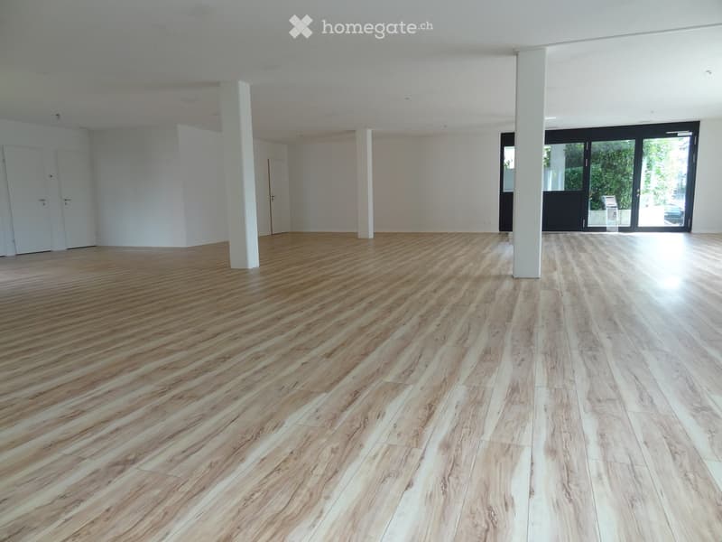 Empty room with wooden flooring, white walls, and large glass doors leading to an outdoor area.