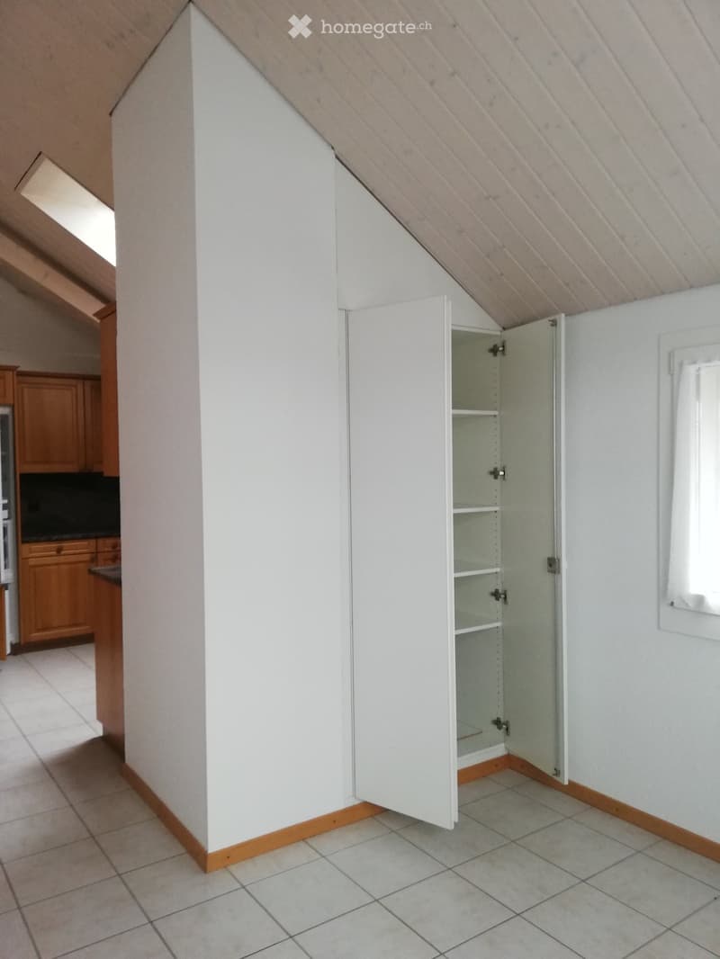 Empty room with white walls, tiled floor, and an open white cabinet with shelves. Wooden trim around the base of the walls and a small window on the right side.