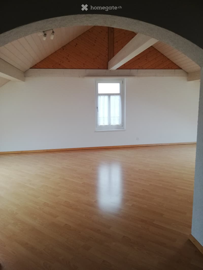 Empty room with wooden flooring, white walls, and a small window with white frame. Exposed wooden beams on the ceiling.