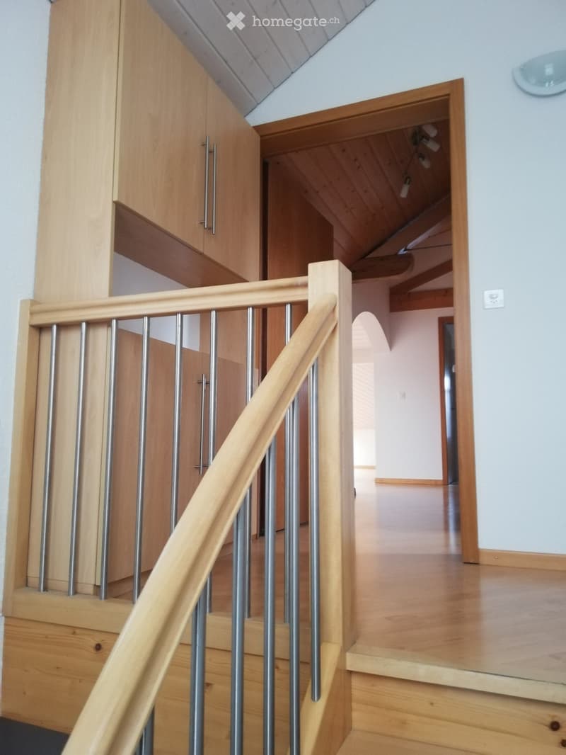 Wooden staircase with metal balusters and wooden handrail, leading to an open area with wooden flooring and white walls.