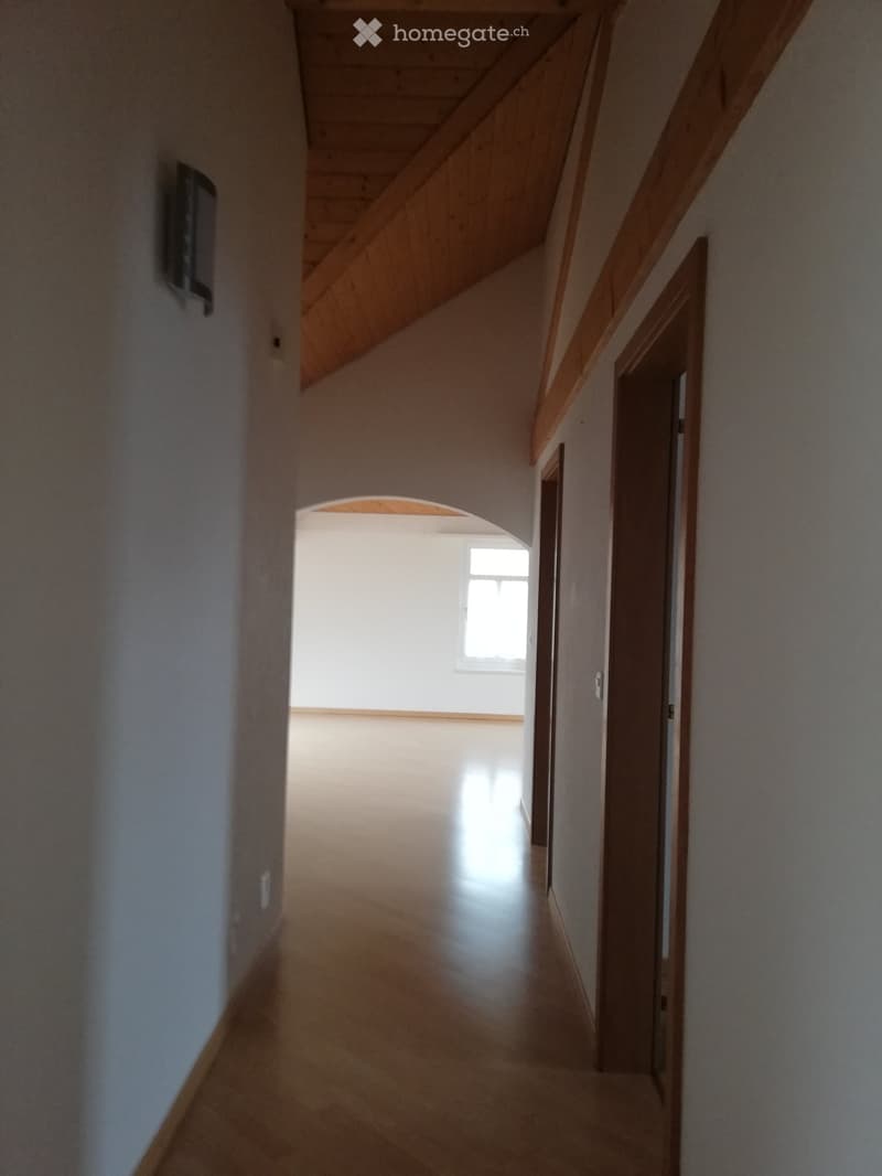 Empty hallway with wooden ceiling beams, light-colored walls, and a door leading to another room.