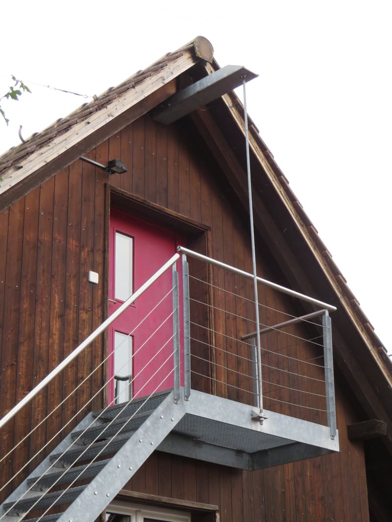 Wooden building with a metal staircase leading to a balcony or terrace, featuring a red door and a railing.
