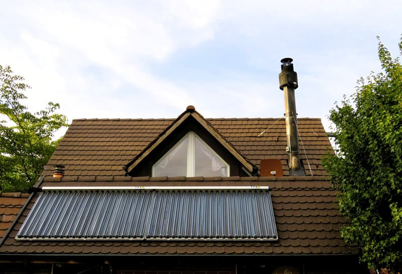 Roof with brown tiles, solar panels, chimney, and dormer window.