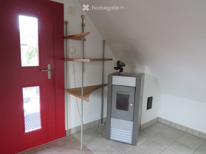 A narrow hallway with a red door, a small wooden shelf unit, and a grey appliance with a fan on top.