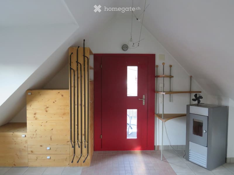 An attic room with slanted ceilings, a red door with windows, wooden built-in storage units, and a small heating unit.