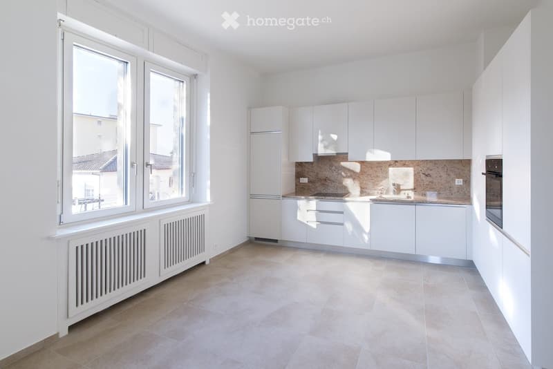 Modern kitchen with white cabinets, a sink, and an oven, featuring large windows and tiled flooring.