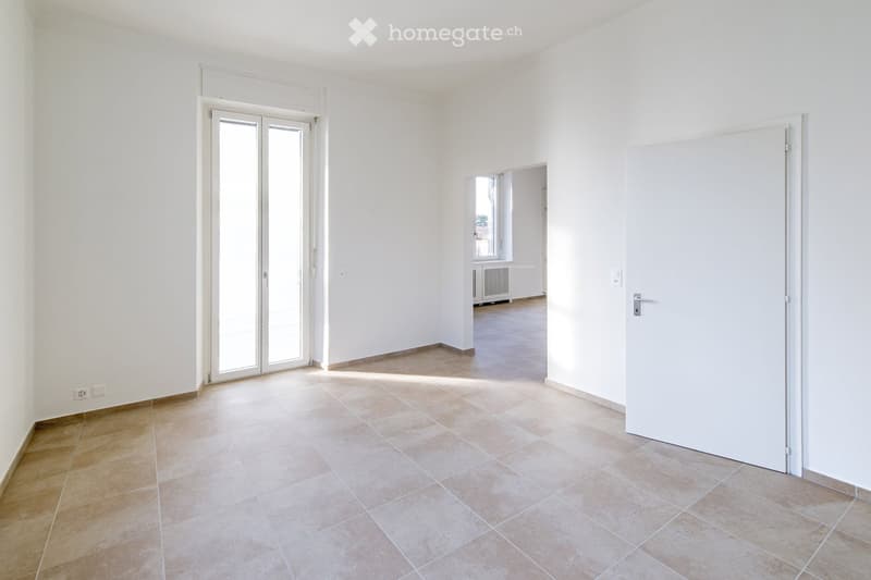 Empty room with white walls, tiled floor, and a large glass door leading to another space.