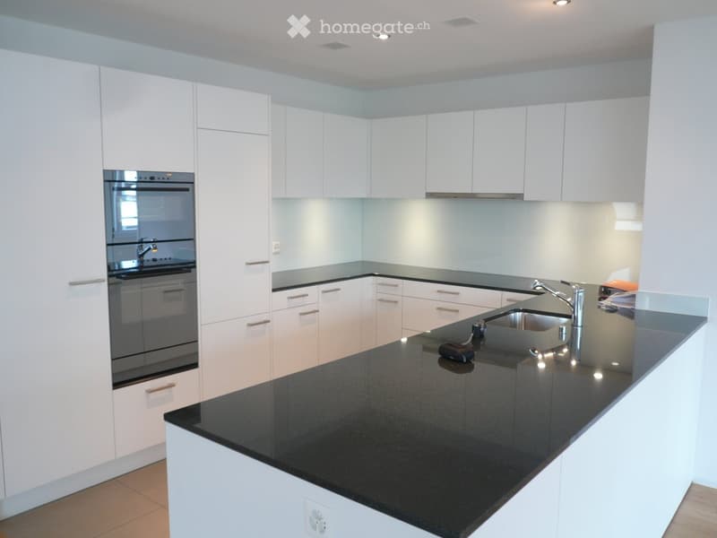 Modern kitchen with white cabinets, black granite countertop, stainless steel sink, and built-in oven.