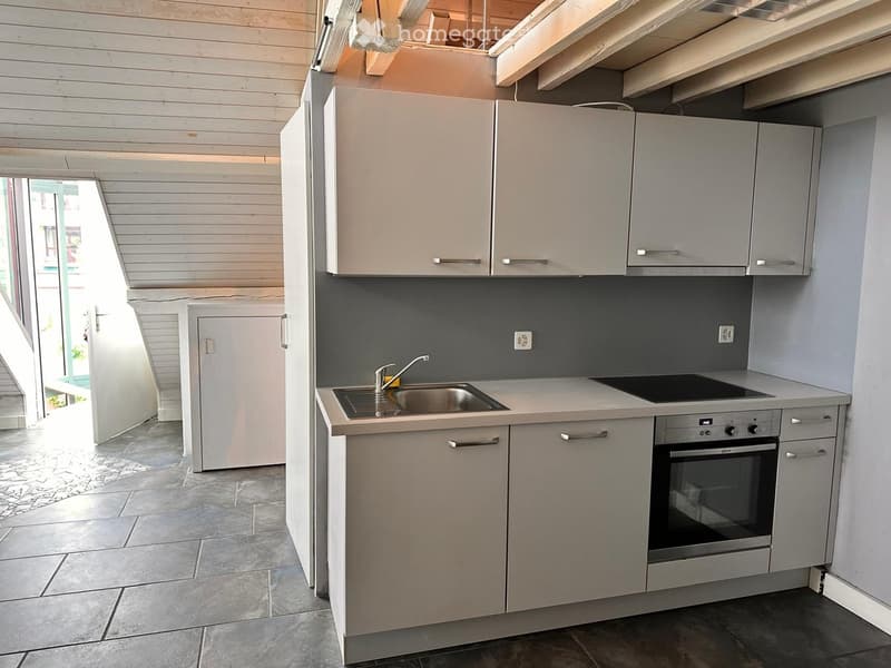 Modern kitchen with light grey cabinets, stainless steel sink, faucet, and built-in oven. Wooden ceiling and tiled floor.